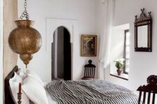 47 a Moroccan bedroom with a black bed with black and white bedding, metal Moroccan lamps and dark-stained furniture