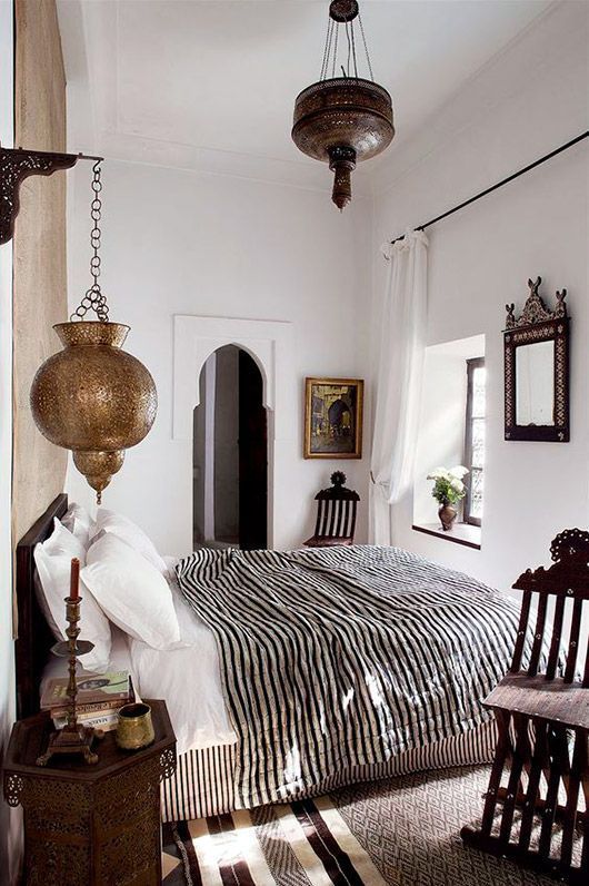 a Moroccan bedroom with a black bed with black and white bedding, metal Moroccan lamps and dark stained furniture