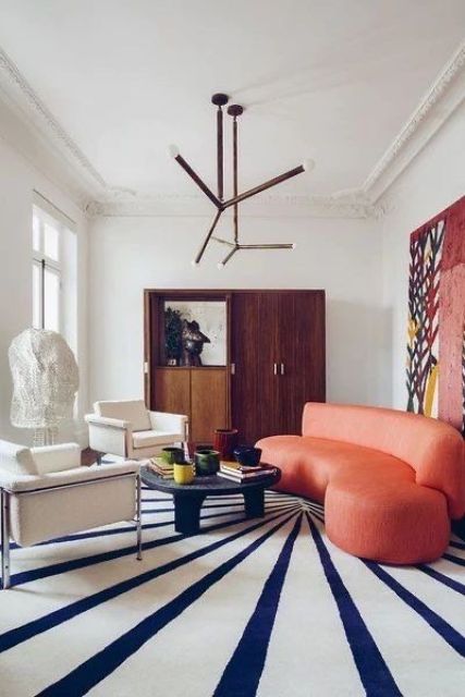 a stained storage unit, a coral curved sofa, a low coffee table, a couple of neutral chairs and a large striped rug