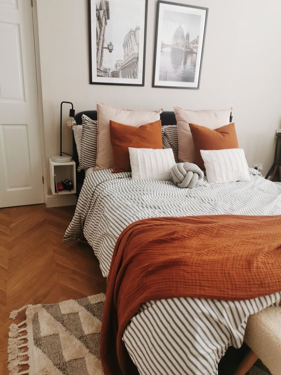 a welcoming bedroom with a black bed, rust and striped grey bedding, a printed rug and a mini gallery wall