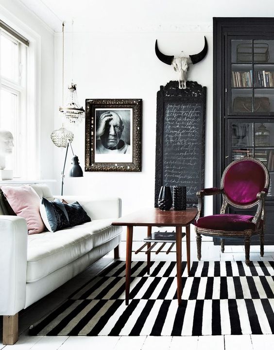 an eclectic living room with a white sofa, a stained table, a purple chair, a striped rug and a black bookcase is wow