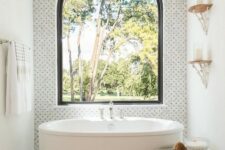 54 a bold bathroom with marble tiles and an arched window for an accent, an oval tub, a beaded chandelier and a rope side table