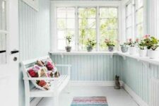 a Scandinavian sunroom clad with mint blue beadboard, with a white bench and bold textiles, potted blooms
