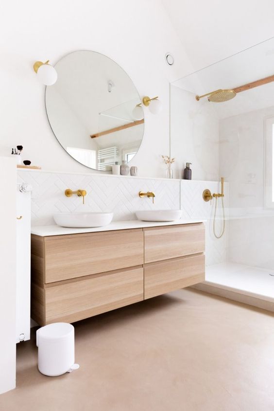 a beautiful contemporary bathroom with white tiles, a large shower space, a floating timber vanity, a round mirror and gold fixtures