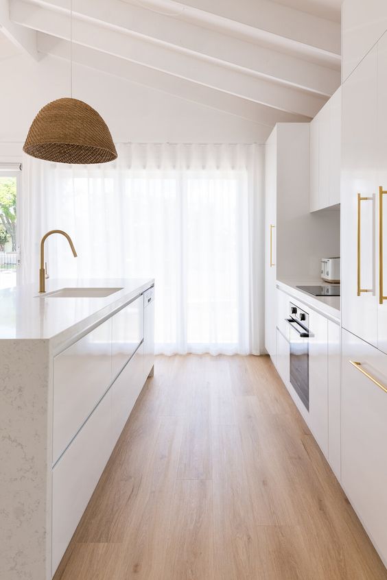 a beautiful contemporary kitchen in white, with sleek cabinets, white stone countertops, gold fixtures and a woven pendant lamp