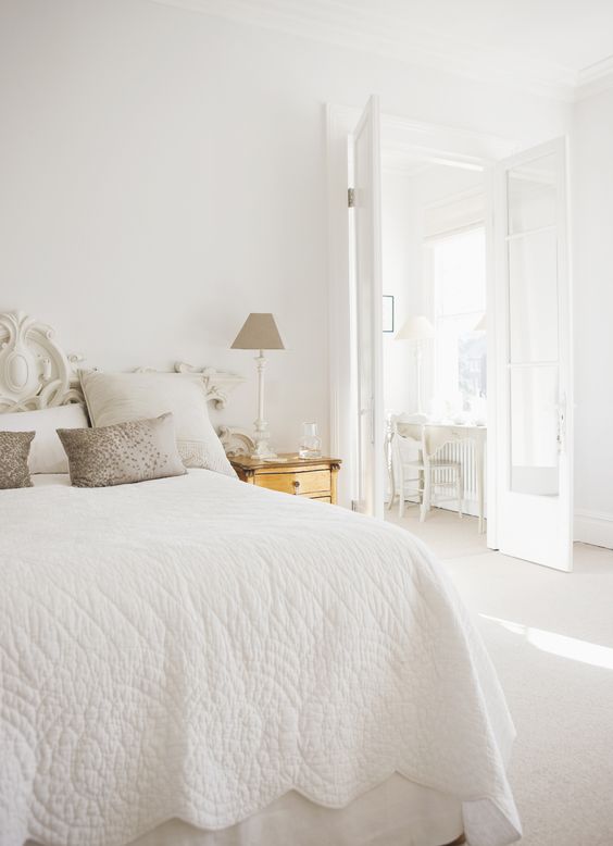 a beautiful white bedroom with a vintage bed and white bedding, a gold nightstand, a neutral lamp is a lovely idea