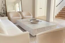 a beautiful white living room with a white sofa and creamy chairs, a low stone slab coffee table and a large floor mirror