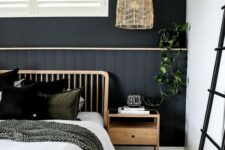 a boho bedroom with a black statement wall done with beadboard, wooden items, comfy layered textiles and greenery