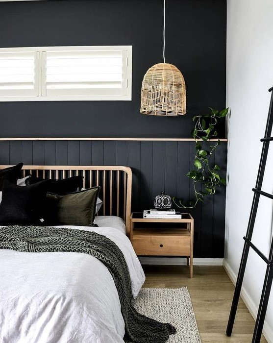 a boho bedroom with a black statement wall done with beadboard, wooden items, comfy layered textiles and greenery