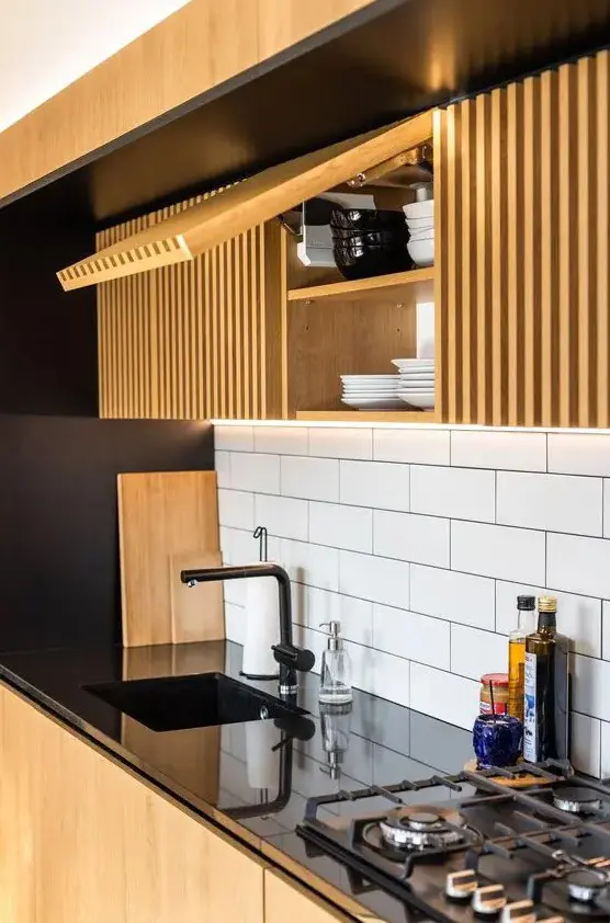 a bold and contrasting kitchen with sleek black surfaces that are juxtaposed to light stained ribbed cabinets