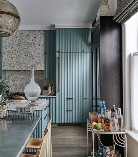 a bright turquoise fluted kitchen with a terrazzo hood, backsplash and countertops, black fixtures and a pendant lamp