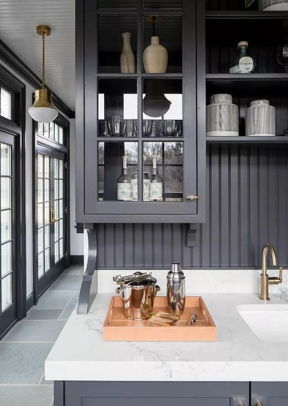 a charcoal grey kitchen with elegant glass facade cabinets, a black beadboard backsplash, a white stone countertop