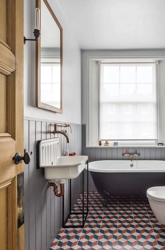 a chic bathroom inspried by vintage, with grey beadboard, a black tub, a vintage sink and a large window with shades