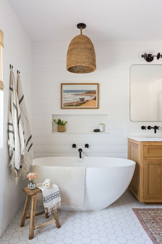 a chic beach bathroom done with a white beadboard wall, hex tiles, a wicker lamp and a wooden vanity plus touches of black