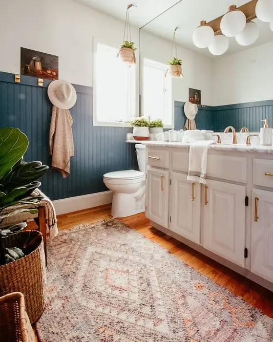 a chic boho bathroom with blue beadboard, a large vanity and a mirror wall, potted plants and layered rugs