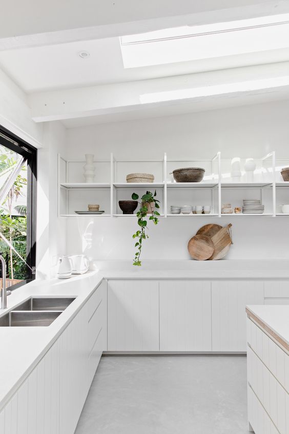 a chic modern kitchen in white, with sleek cabinetry, an open shelving unit instead of upper cabinets and skylights