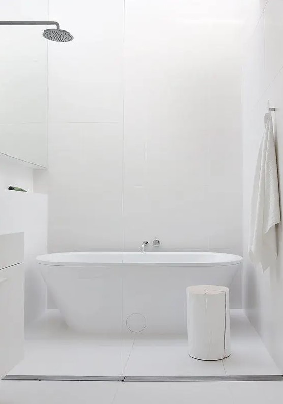 a chic white bathroom with a free standing bathtub, a whitewashed stool and minimalist furniture