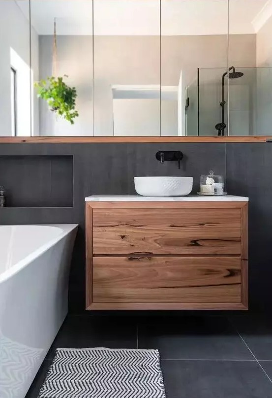 a contemporary bathroom clad with concrete tiles, a floating vanity, a mirror storage unit, a bathtub and niches for storage