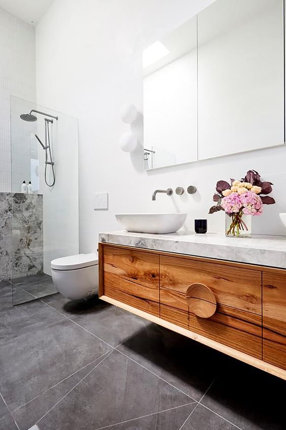 a contemporary bathroom clad with grey tiles, a floating timber vanity with a stone countertop, a mirror cabinet and a shower space