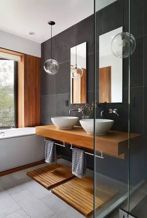 a contemporary bathroom clad with grey tiles of various shades, a bathtub, a floating vanity, wooden mats and accents