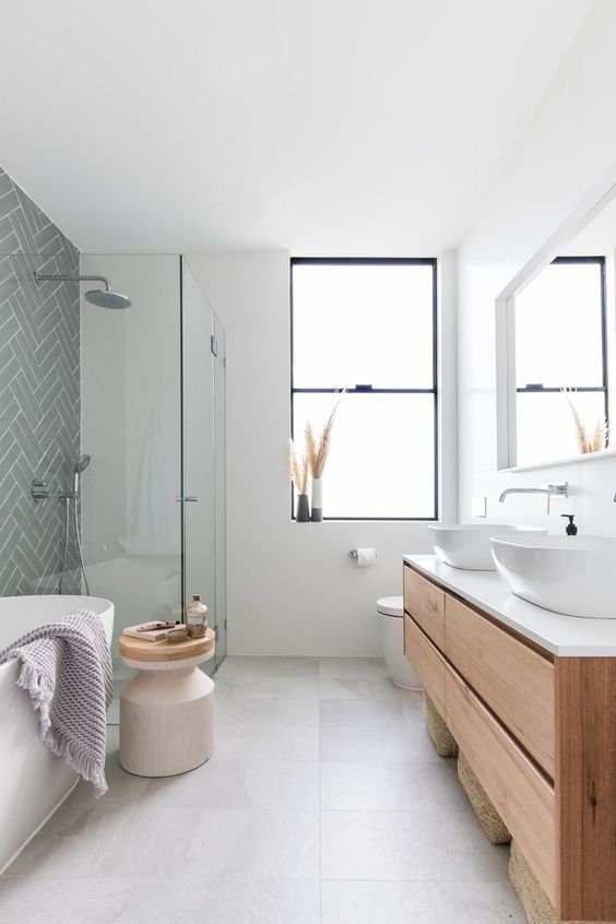 a contemporary bathroom in neutrals, with a grey tile wall, a tub, a side table, a floating timber vanity and two sinks