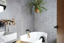a contemporary bathroom with large scale concrete and geometric tiles, an oval tub, a floating vanity and a white marble sink plus greenery