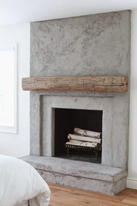 a contemporary concrete fireplace with a rough wood mantel and firewood in the fireplace   the mantel cozies the fireplace up