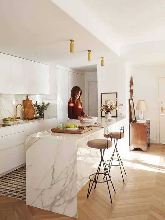 a contemporary white kitchen with sleek cabinets, a white marble kitchen island, matching countertops and a backsplash