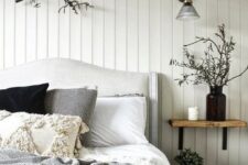 a contrasting bedroom with black walls, white beadboard, an upholstered bed, wooden and wicker touches and branches