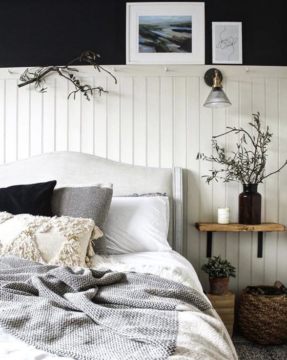 a contrasting bedroom with black walls, white beadboard, an upholstered bed, wooden and wicker touches and branches