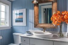 a cool bathroom with blue beadboard walls and a white beadboard ceiling, a white vanity, a mirror in a stained frame