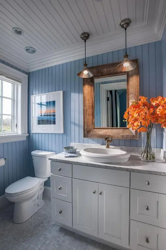a cool bathroom with blue beadboard walls and a white beadboard ceiling, a white vanity, a mirror in a stained frame
