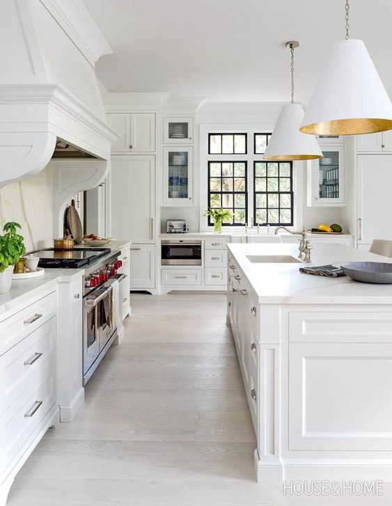 a cool white farmhouse kitchen with shaker cabinets, white stone countertops, white pendant lamps and potted greenery