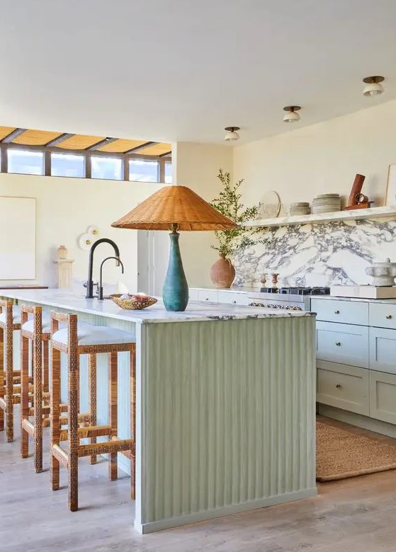 a cozy and welcoming mint green kitchen with shaker style cabinets, an open shelf instead of upper ones, a white marble backsplash, a fluted kitchen island