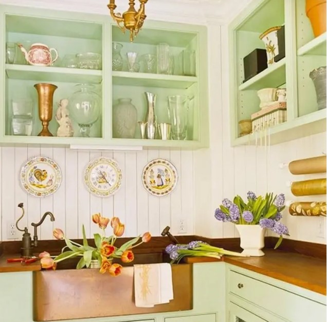 a cozy cottage kitchen with green cabinets and box shelves, a white beadboard backsplash, a copper-colored countertop and a copper sink