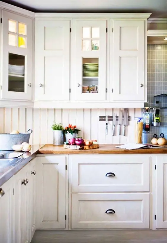 a cozy creamy kitchen with shaker cabinets, a matching beadboard backsplash, butcherblock countertops