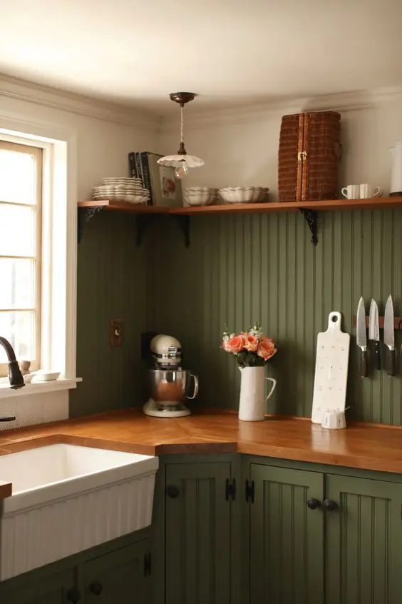 a cozy farmhouse kitchen with green beadboard cabinets and a matching backsplash, butcherblock countertops and a matching open shelf