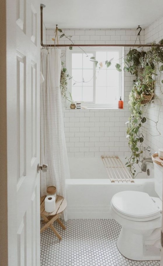 a cozy tiny bathroom clad with marble hex tiles and white subway ones, potted greenery and a wooden stool is a stylish and welcoming space