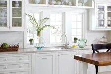 a cozy white kitchen with shaker style cabinets, glass and usual ones, neutral stone countertops, baskets and vases