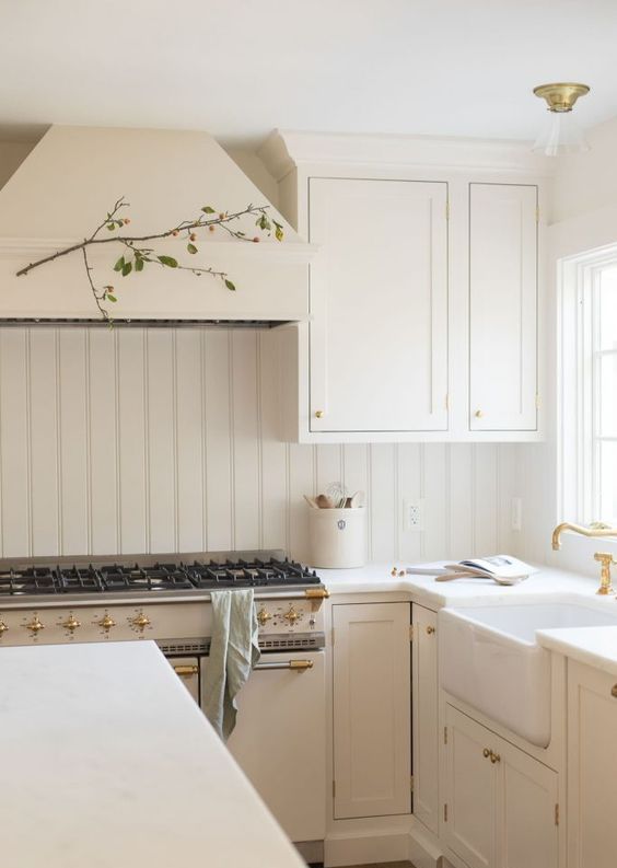 a creamy farmhouse kitchen with shaker cabinets and a matching beadboard backsplash, white stone countertops