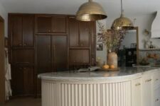 a dark-stained kitchen with a light-colored fluted curved kitchen island that contrasts the cabinetry and stainds out in its backdrop