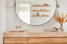 a desert bathroom with a large timber vanity with a pink quartz countertop, a round mirror, open shelves and a bold rug