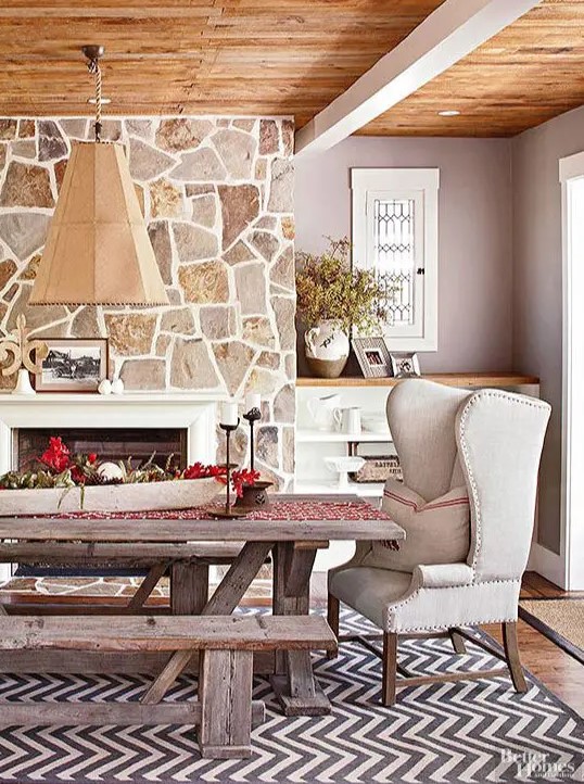 a farmhouse dining space with a fireplace clad with stone, a rough wood ceiling, a built-in storage unit, a rough wood dining set plus an elegant wingback chair
