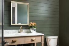 a farmhouse powder room clad with dark green beadboard, a stained vanity, a white countertop, gold touches
