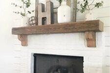 a farmhouse white brick mantel with a rough wood slab mantel, greenery in vases, wooden frames and a wooden basket for firewood