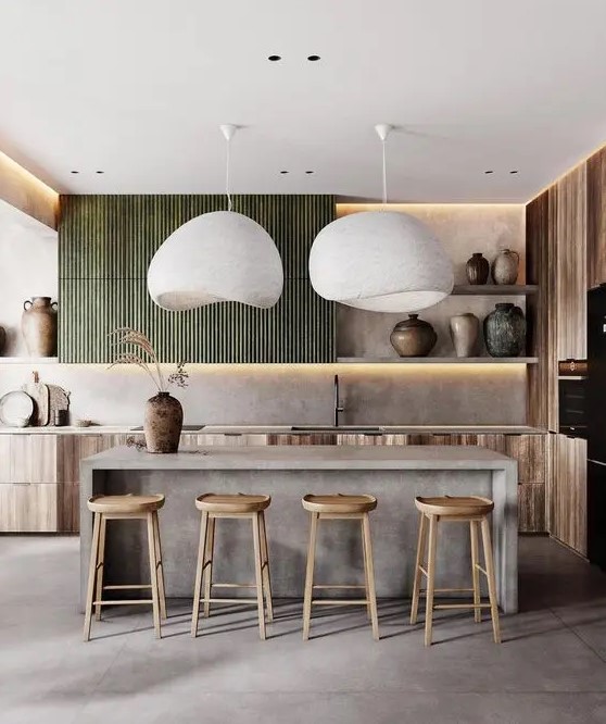 a gorgeous kitchen with stained lower and green fluted upper cabinets, a concrete kitchen island, wooden stools and statement vases