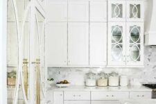 a gorgeous white kitchen with brass details and mirror and glass doors looks really luxurious