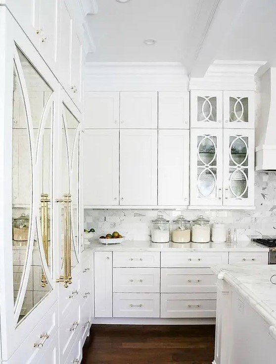 a gorgeous white kitchen with brass details and mirror and glass doors looks really luxurious