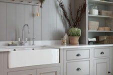 a grey farmhouse kitchen with shaker cabinets, a matching beadboard backsplash and white stone countertops