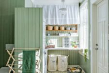 a laundry room clad with green beadboard, with a green tile floor, open shelves and chic vintage chandeliers